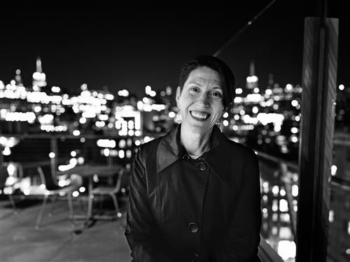 Black & White night image of a woman standing on a patio with a lit city skyline in the background